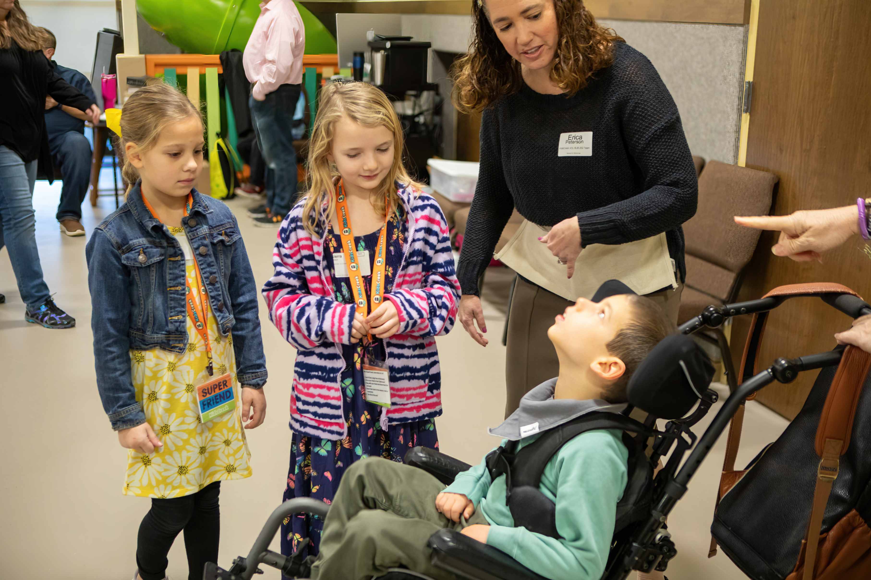 Two children and an adult leader greet a child in a wheelchair.